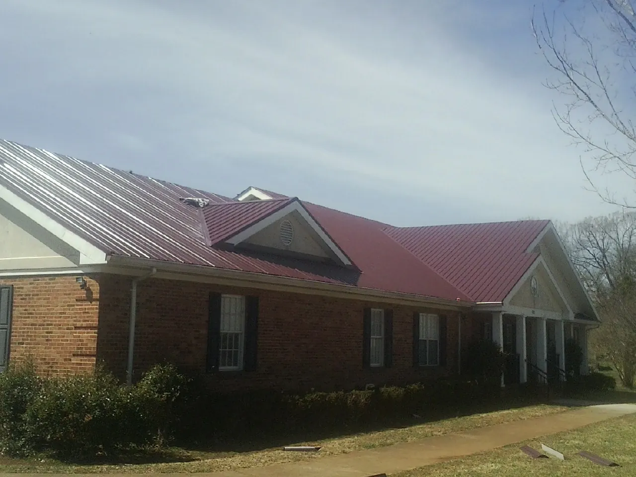 Red metal roof with gabled entries on a long brick building, from a Hail Damage Roof Repair job in Drexel Hill
