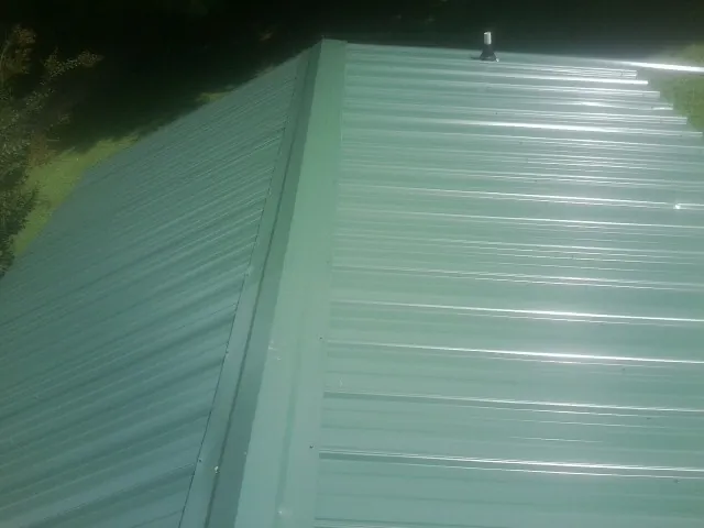 New green metal panels meeting at the ridge of a roof — Flat Roof Repair work by our crew in Drexel Hill