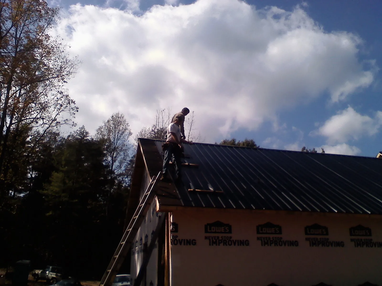 Roofer fastening dark metal panels high against a cloudy sky, from a Roof Inspection job in Drexel Hill