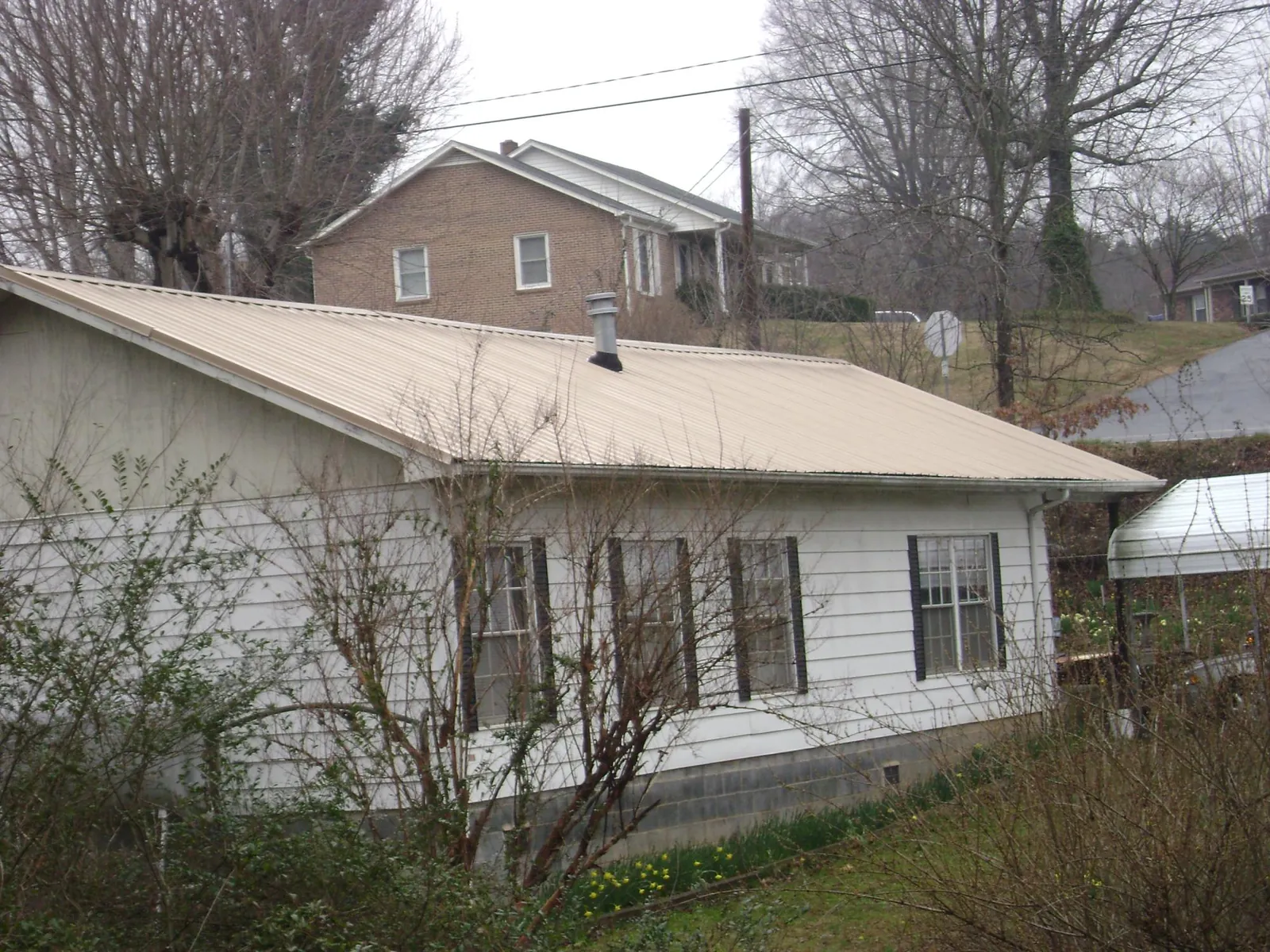 Tan metal roof on a white sided house set into a hillside — Commercial Roofing by Roofing Brothers in Drexel Hill